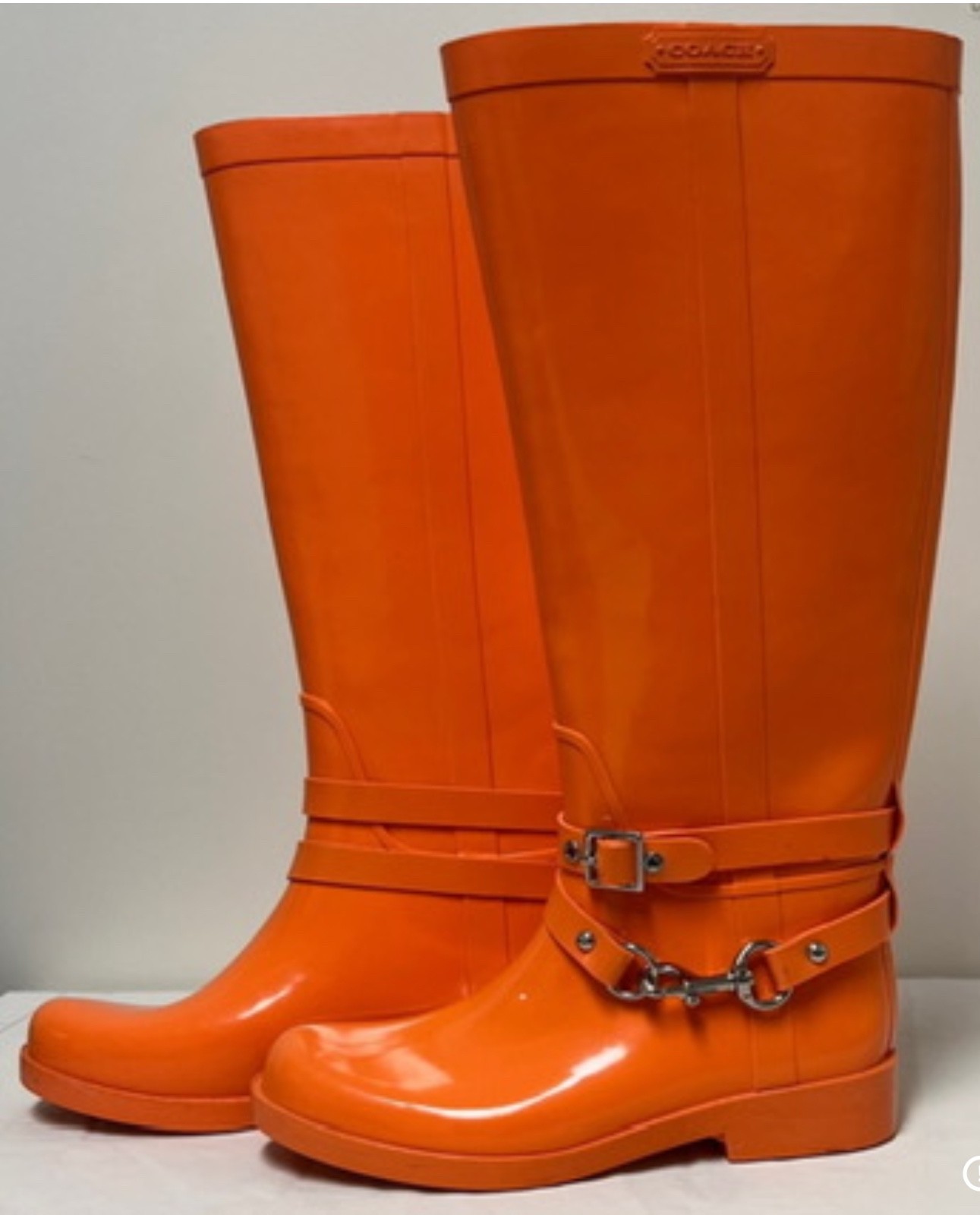 These are authentic Coach Lori tall rain boots in a bold orange color featuring