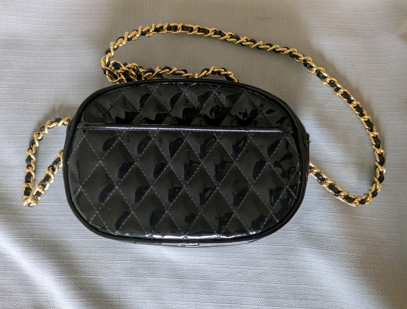 Black Patent Leather Oval Crossbody Bag. Goldtone chain handle with black accent