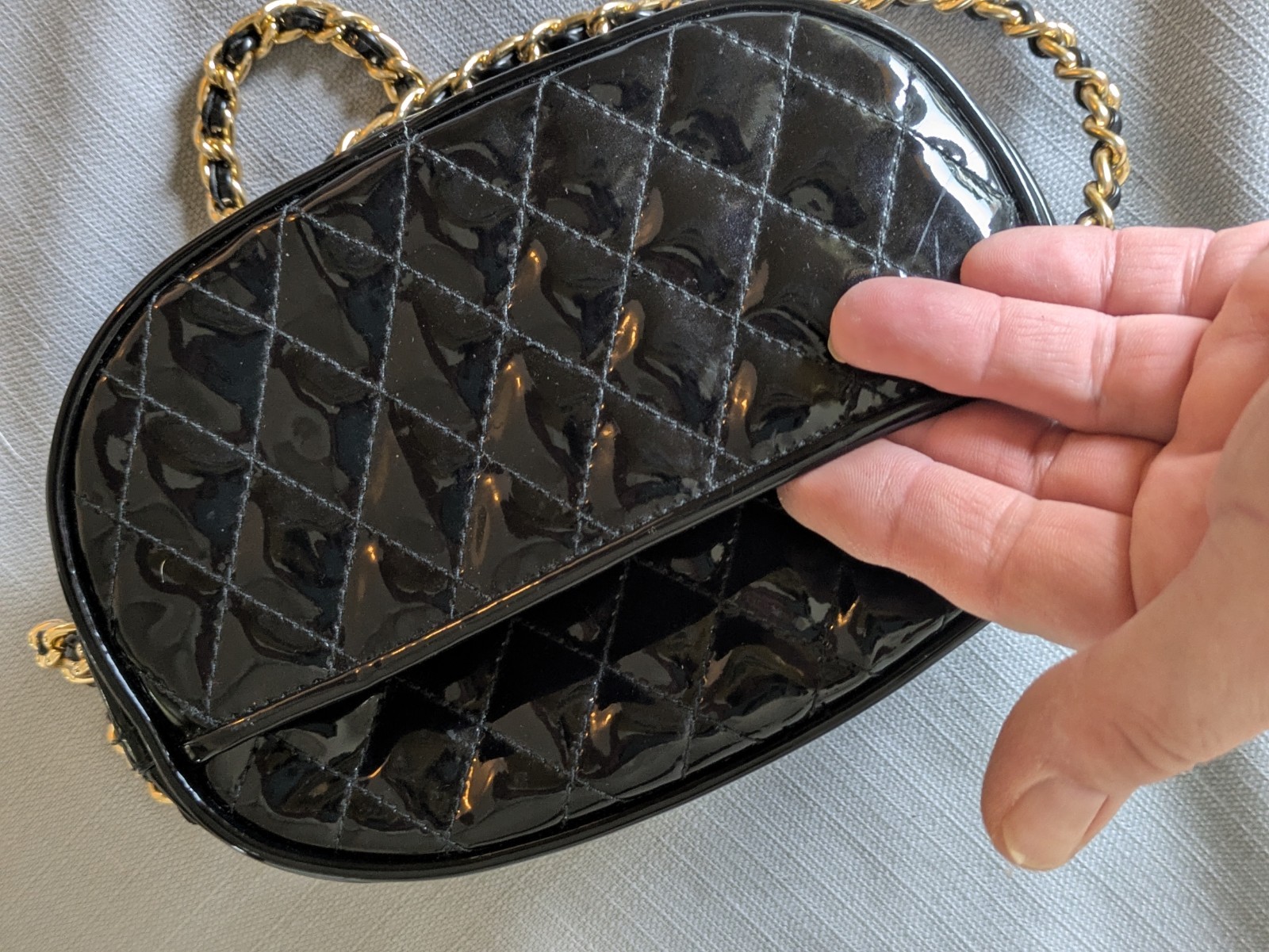 Black Patent Leather Oval Crossbody Bag. Goldtone chain handle with black accent