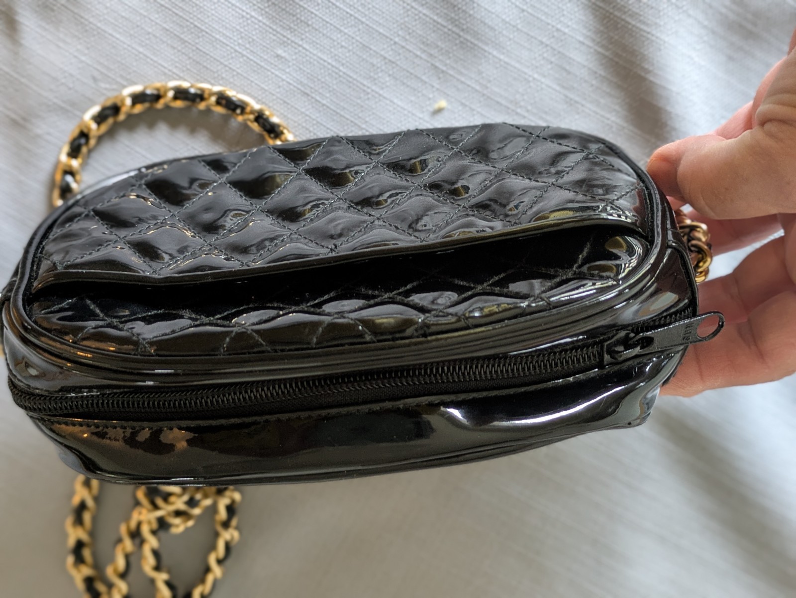 Black Patent Leather Oval Crossbody Bag. Goldtone chain handle with black accent