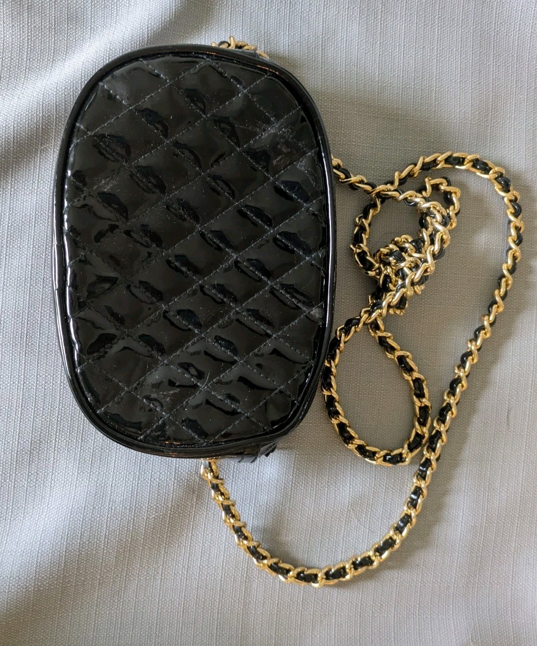 Black Patent Leather Oval Crossbody Bag. Goldtone chain handle with black accent